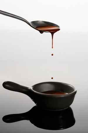 Melted milky brown chocolate pouring from a spoon, isolated on whiteの写真素材