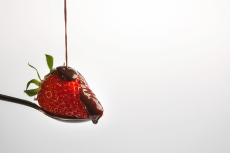 A Strawberry sitting on a spoon gets Chocolate Syrup dropped on it. isolated white. with copy spaceの写真素材