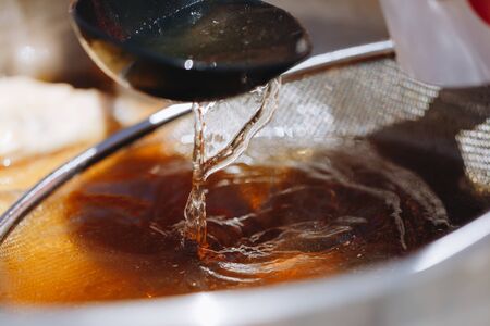 fresh broth in a saucepan through a sieve in a ladleの写真素材