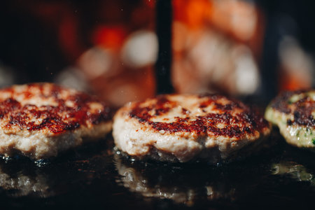 Some patties of ground meat with a flame in the front on cooking grate.の写真素材