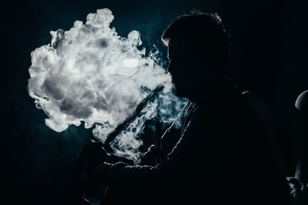 silhouette of a man exhaling smoke on a dark background closeup