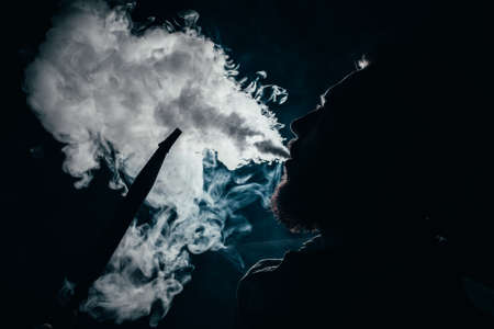 silhouette of a man exhaling smoke on a dark background closeupの写真素材