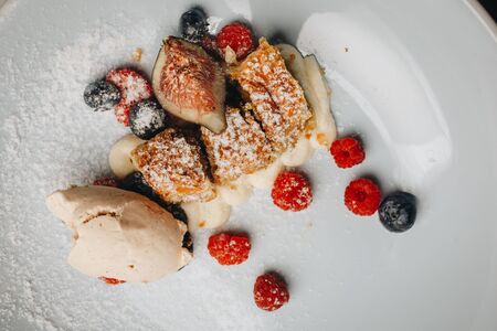 Strudel with raisins, fresh berries and ice cream. Slices of strudel with raisins and apples, sprinkle with powdered sugar on a white plate with fresh berriesの写真素材