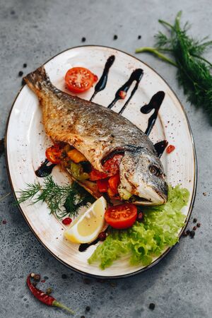 Dorado grilled stuffed with vegetables on a white plate on a gray background with copy spaceの写真素材