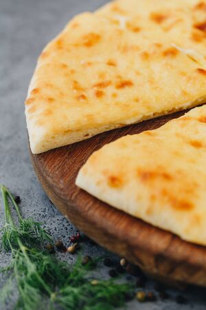 Sliced pie with cheese on a wooden board on grey background. Khachapuri.の写真素材