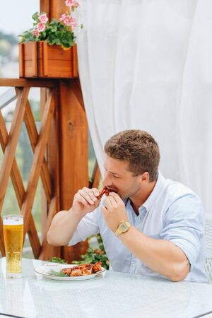 guy eats grilled chicken wings and drinks beer in a restaurant.の写真素材