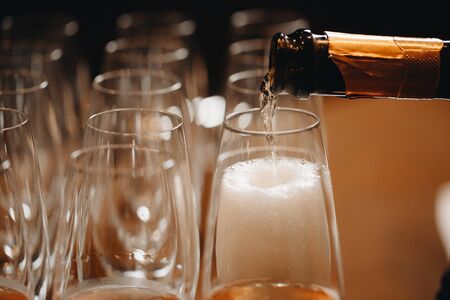 Pouring champagne into wine glasses. Champagne flutes on a wedding or new year eve party.の写真素材