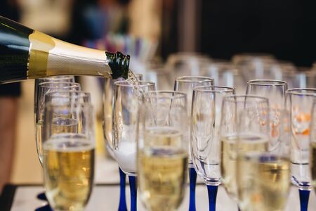 Pouring champagne into wine glasses. Champagne flutes on a wedding or new year eve party.の写真素材