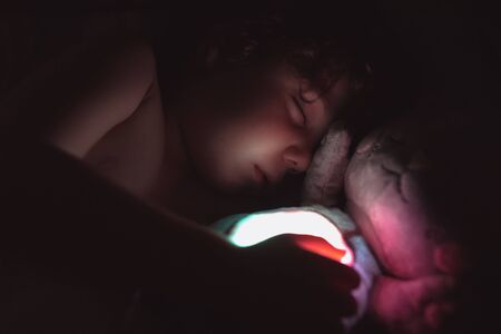 Little boy sleeps nonchalantly in a hug with a toy at night.の写真素材