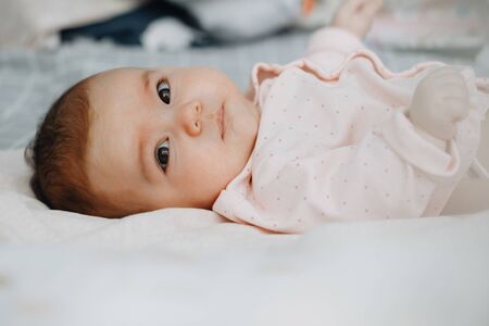 baby girl lying on her back on the bed in a bright bedroom, dressed in a light sundress. calm baby baby 3 months old. copy space.の写真素材