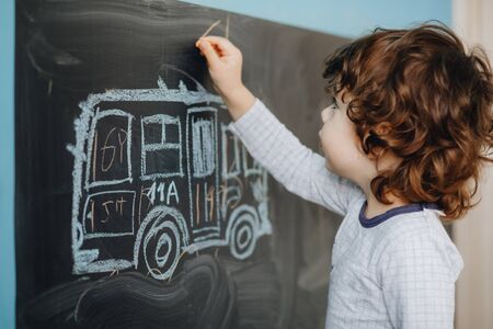 Curly little boy draws chalk on a board in his room.の写真素材