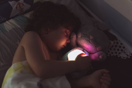 Little boy sleeps nonchalantly in a hug with a toy at night.の写真素材