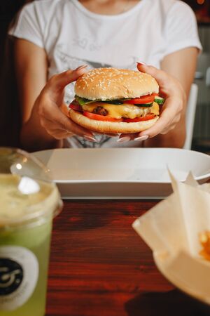 tasty burger. stylish hipster woman holding juicy hamburger in hands close up. boho girl with hamburger at cafe food festivalの写真素材
