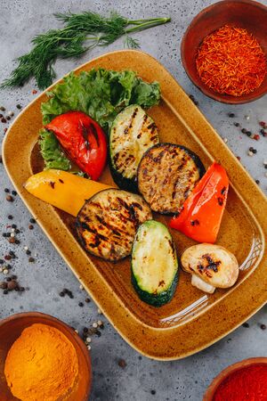 hot delicious grilled vegetables on a brown ceramic plate on a grey background.の写真素材