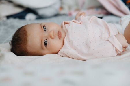 baby girl lying on her back on the bed in a bright bedroom, dressed in a light sundress. calm baby baby 3 months old. copy space.の写真素材