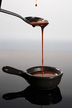 Melted milky brown chocolate pouring from a spoon, isolated on white.の写真素材