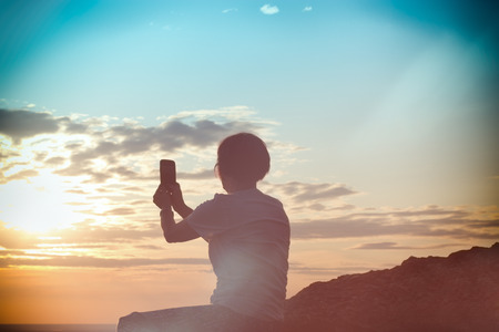 Woman enjoys in sunset view and taking photo by mobile phoneの写真素材