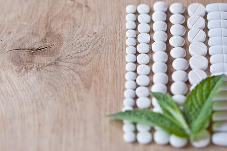 White pills and foliage mint on a wooden backgroundの写真素材
