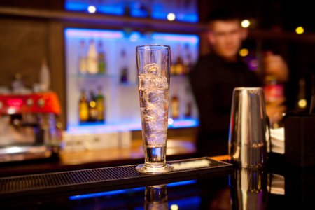Tall glass with ice cubes on the bar counter.