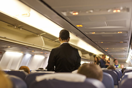 Interior of airplane with passengers  and stewardess walking the aisle.