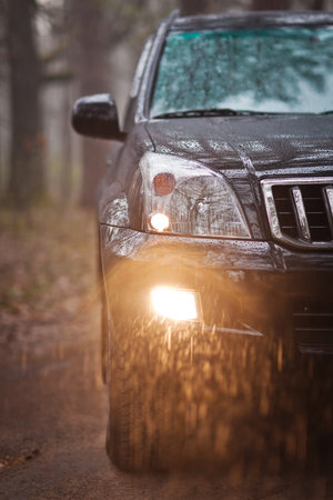 Close-up photo front side of the black SUV in forest at rain
