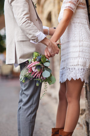 A guy holding a girl by the hand with a bouquet of flowers.