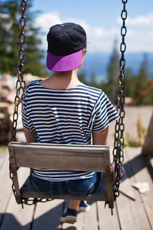 A young girl is riding on a swing overlooking the mountains.の写真素材