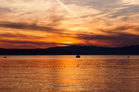 Orange sunset on the sea with the sun, a beautiful sky on the background of mountains.の写真素材