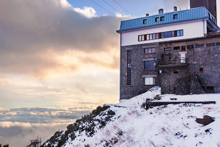 A stone building stands on a cliff of a mountain above the clouds.