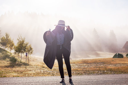 Young girl in a raincoat in the morning at dawn against a background of fog and mountains