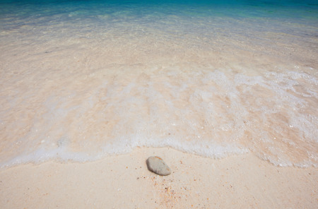 Wave of the sea on the sand beach and single stoneの写真素材