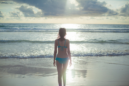 Young woman walk on an empty wild beach towards celestial beams of light falling from the skyの写真素材