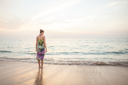 Young woman walk on an empty wild beach towards celestial beams of light falling from the skyの写真素材