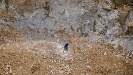 Construction worker electric drill Drilling mountain ground in construction area with rock mountain backgroundの写真素材