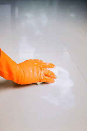 A female hand in a yellow latex glove sponges a tile. There is a lot of foam in the floor. The concept of cleaning the bathroom or kitchen, cleanliness. Copyspace.の写真素材