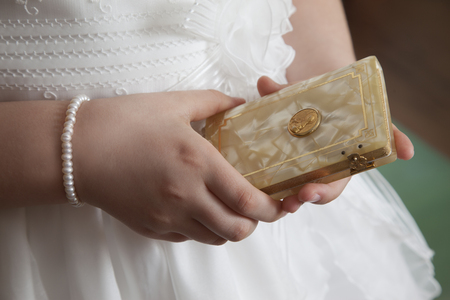 detail of a first communion girl dressed in white with bracelet watch and book in her handsの写真素材