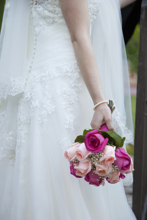detail of the bridal bouquet in salmon and pink colors, which holds the bride placed on her back, wearing her white dressの写真素材