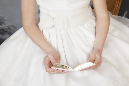 detail of communion hands of a girl dressed in white with a book in her handの写真素材