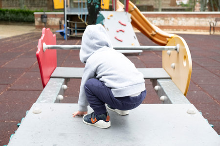 Child under two years playing in the park wearing a gray jacket whit hood and blue trousers,with his...