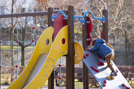 two year old boy playing in an outdoor park on a sunny winter day,dressed in a blue coat and brown trousersの写真素材
