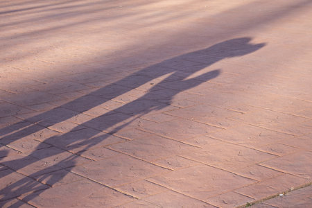 two year old boy riding a blue bike without pedals on a cold but sunny winter day where you can see his shadow projected on the ground.The boy is dressed in a blue coat with a hood and brown trousers with green gloves in his handsの写真素材