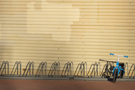 Two years old boy parking his blue bicycle without pedals in a bike park, on a cold and sunny day in the late fall early winter. he is dressed in a blue hooded coat, brown pants, green gloves and scarfの写真素材