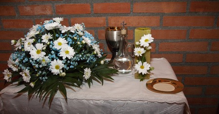 detail of the table of the offering on the day of the first communion of a group of boys and girls. where you can see, a center of white and blue flowers, the quality of wine, a candle adorned with white daisies that symbolizes light, the body of Christ in the form of bread, and a jug of water that symbolizes purity.の写真素材