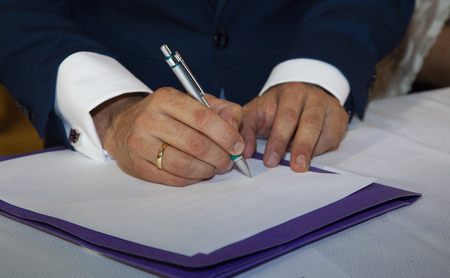 detail of the grooms hands when signing the marriage certificate, holding a pen and wearing his wedding band.の写真素材