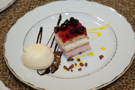 flat detail of a strawberry and forest fruit cake with a vanilla ice cream ball decorated with chocolate a white plate decorated with a golden border.の写真素材