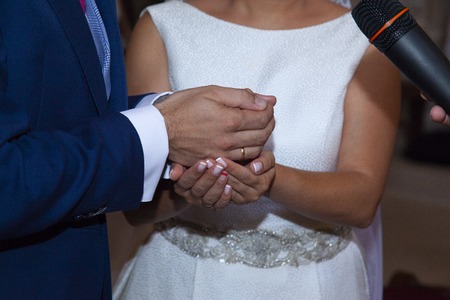 detail of the hands of the bride and groom just at the moment in which the bride gives the arras as a symbol of the goods that are going to share the groom wearing a suit of blueの写真素材