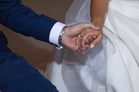 detail of the hands of the couple during the church ceremony where you can see that the groom is wearing a blue suits and the bride a nice white dress with painted nailsの写真素材