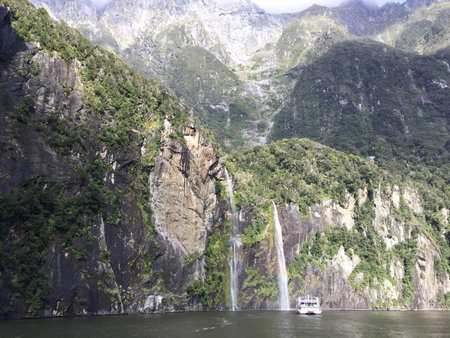 Waterfall from mountain top with rainbow and scenic cruise ferry boat, New Zealandの写真素材