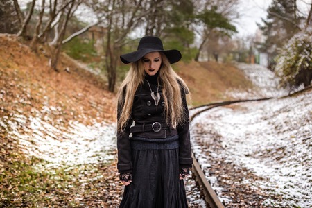 Woman in long black dress and hat walking on railway tracks. Winter. Cold weather. Travel alone.の写真素材