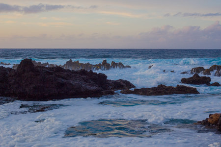 Lava stones on the beach of Piscinas Naturais Biscoitos. Atlantic Ocean. Natural pool with sea foam...